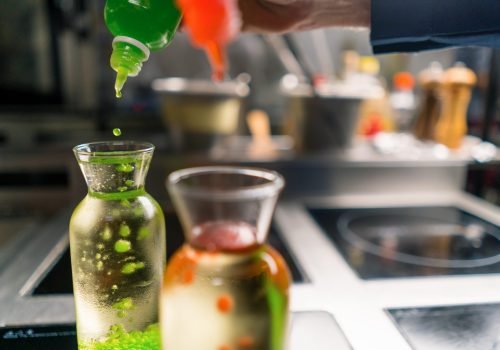 a chef in a professional kitchen experiments by adding multi-colored molecular caviar grains to container with water close-up